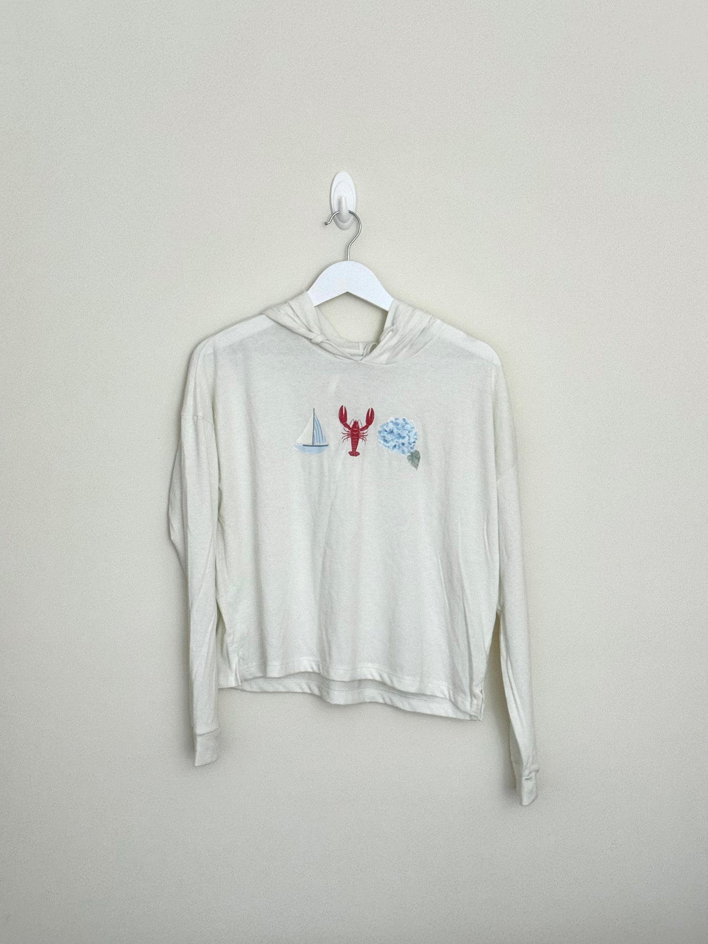 Beige long-sleeve shirt with graphic design on a hanger against a beige background