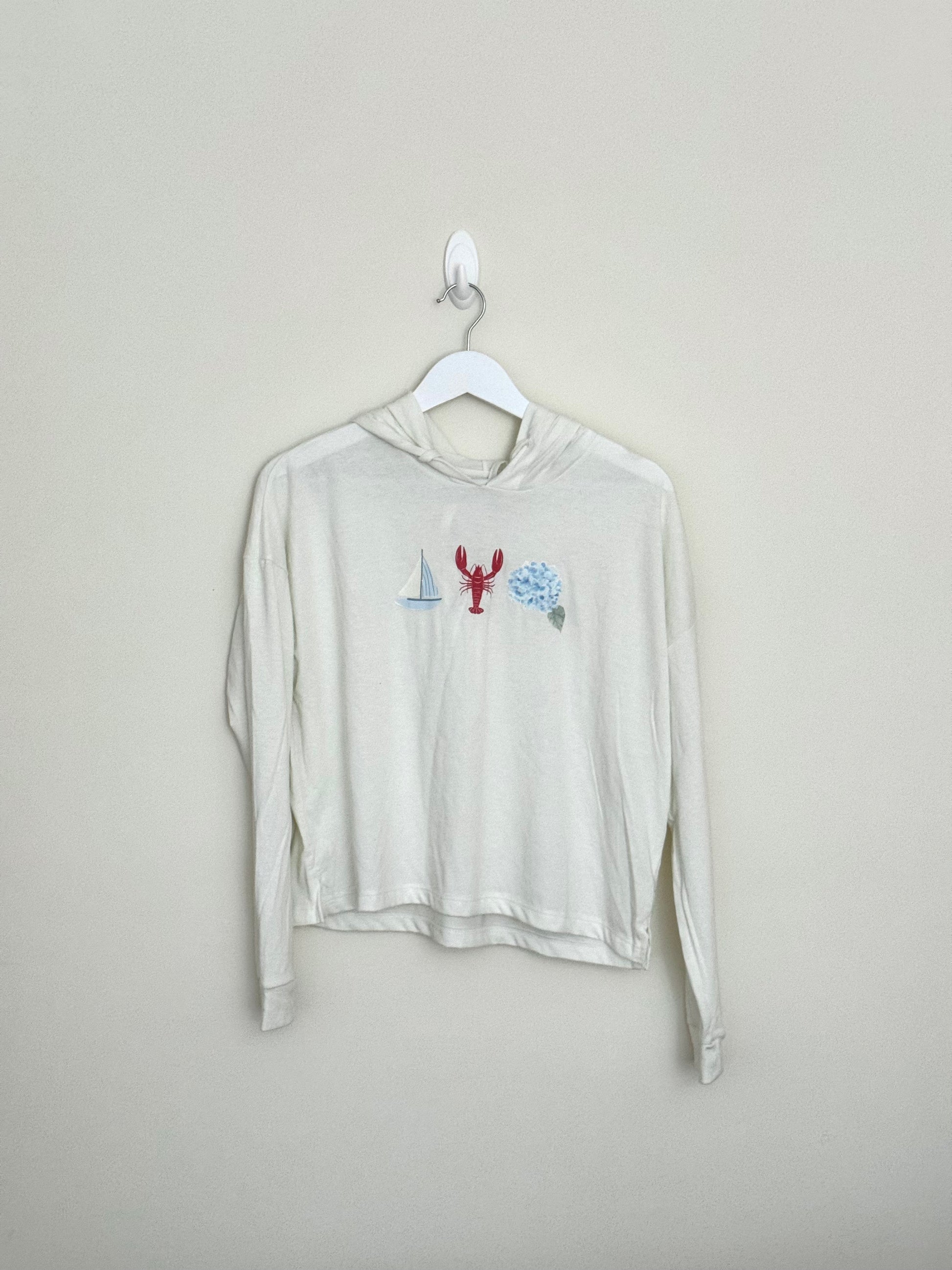 Beige long-sleeve shirt with graphic design on a hanger against a beige background