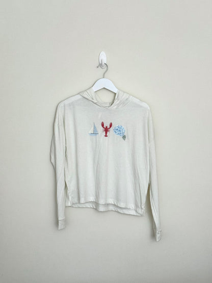 Beige long-sleeve shirt with graphic design on a hanger against a beige background
