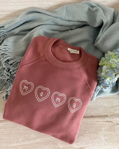 Folded pink sweatshirt with heart designs on a wooden surface with a blue scarf and flowers.