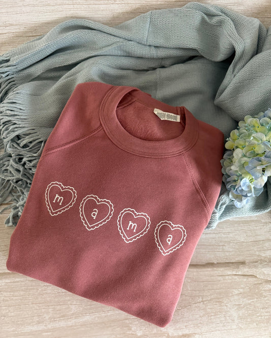 Folded pink sweatshirt with heart designs on a wooden surface with a blue scarf and flowers.