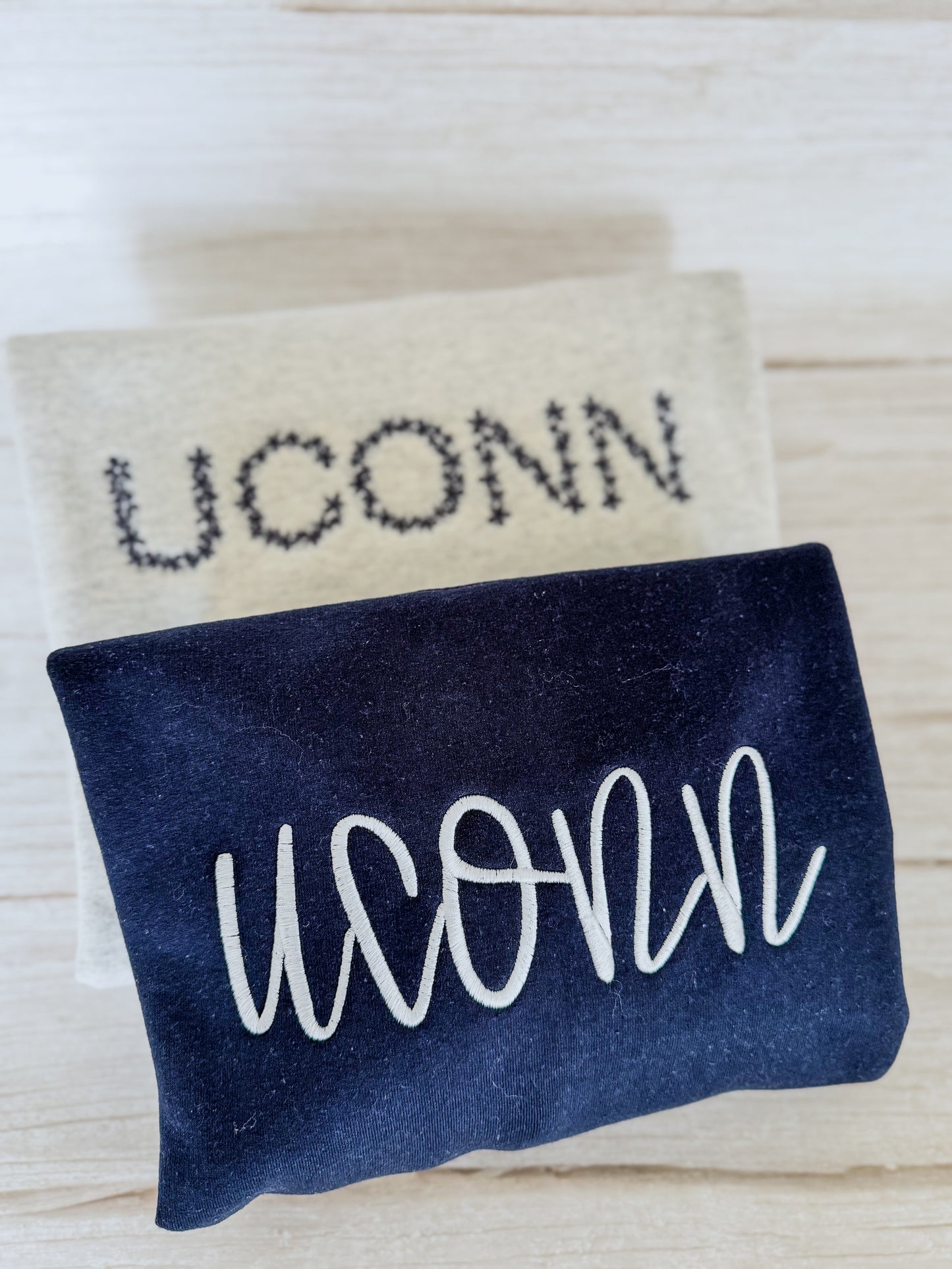 Two versions of a sweatshirt with 'UCONN' text on a light wooden surface