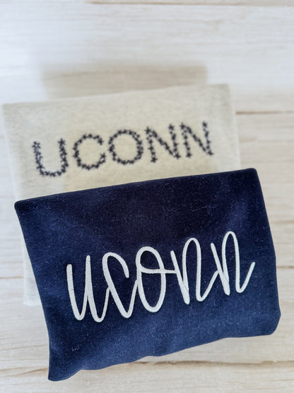 Two versions of a sweatshirt with 'UCONN' text on a light wooden surface