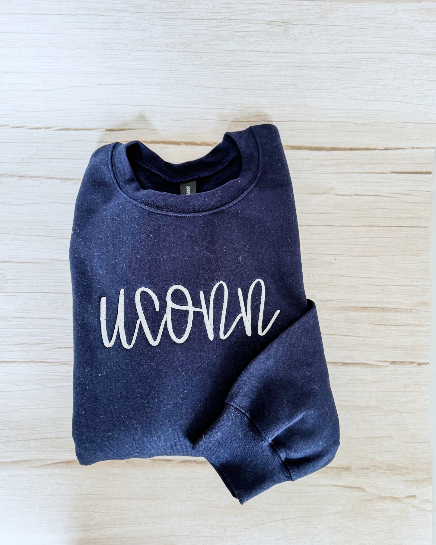 Folded navy blue sweatshirt with 'UCONN' text on a light wooden surface