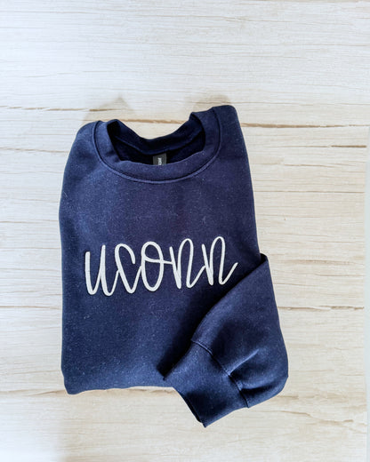 Folded navy blue sweatshirt with 'UCONN' text on a light wooden surface
